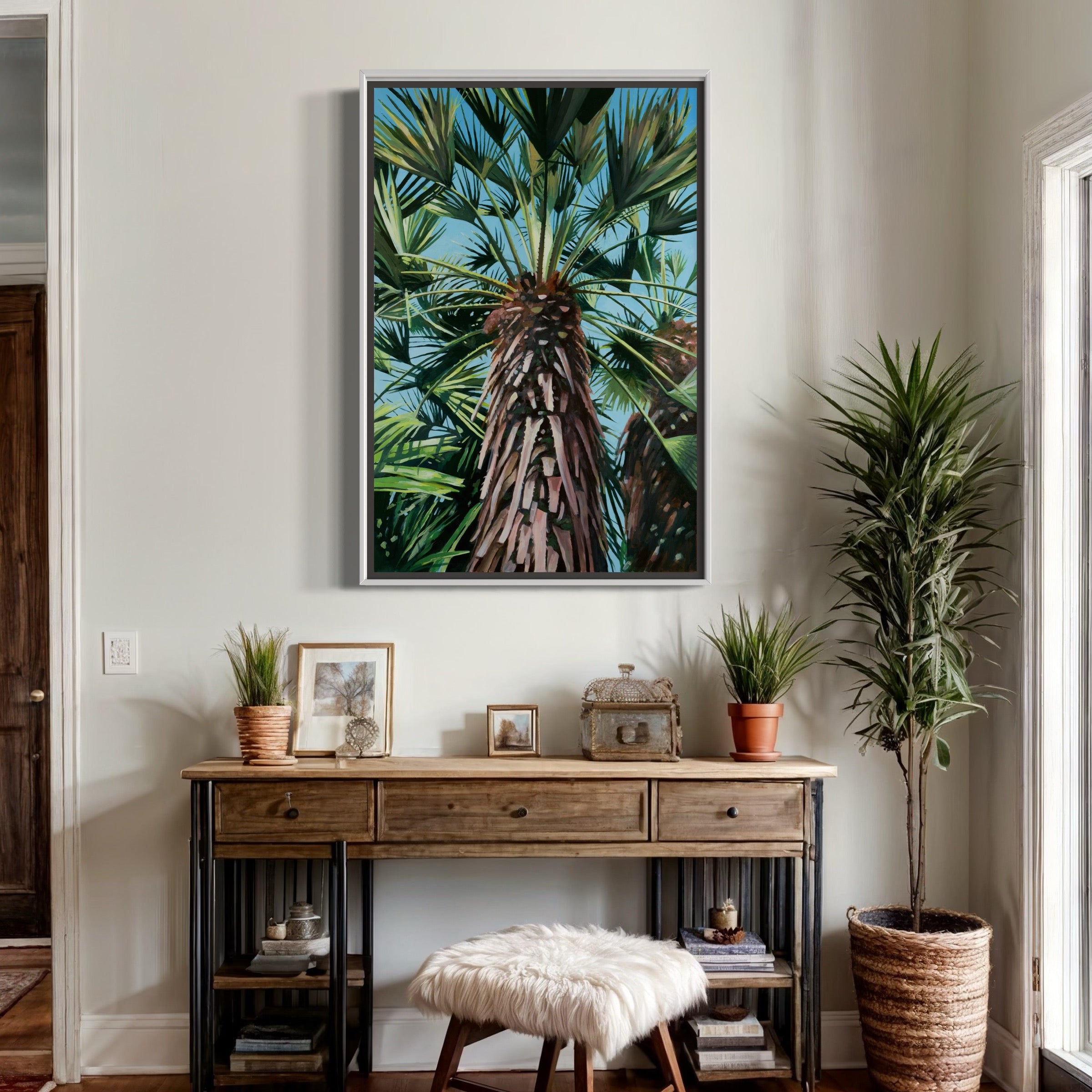 A framed canvas print of a palm tree displayed on a wall above a wooden table with various decorative items and plants.